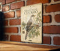 A vintage-style metal plaque with an illustration of a yellow-billed cuckoo bird on a branch, mounted on a brick wall.