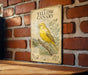 A vintage-style poster of a yellow canary is displayed on a brick wall, featuring an illustration of the bird perched on a branch.