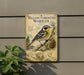 A vintage-style metal sign with a bird illustration, mounted on a wall next to a plant.