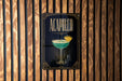 a poster or sign with the word "ACAPULCO" prominently displayed, along with an illustration of a cocktail glass containing a green drink and a slice of lemon.