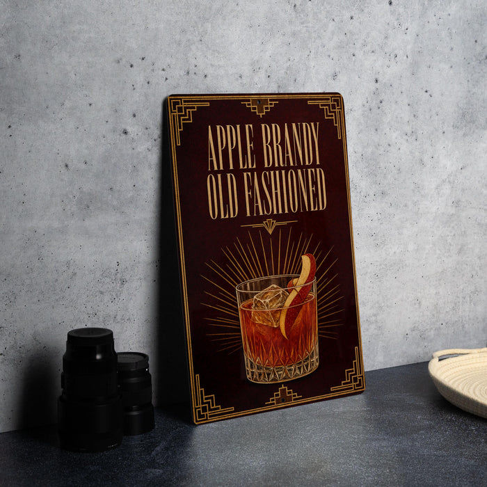 a sign with the text "APPLE BRANDY OLD FASHIONED" and an illustration of a glass of amber-colored liquid with a slice of apple on top.