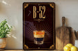 a sign with the text "B-52" and an illustration of a layered drink, likely a cocktail or mixed drink, with a glass in the center. The sign is displayed on a wall, and there are some kitchen items, such as a cutting board and a bowl, visible in the background.