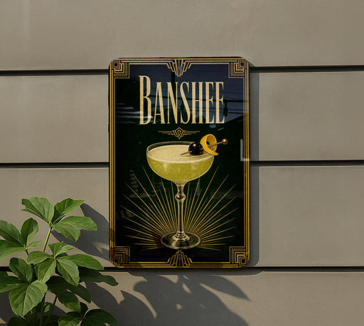 A framed poster of a cocktail with a lemon on top, hanging on a wall next to a plant.