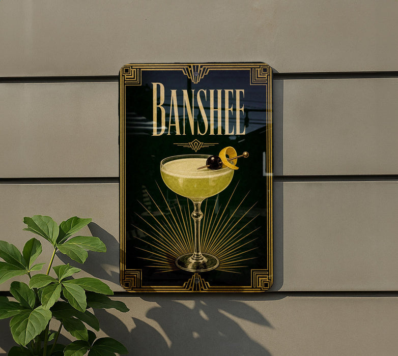 A framed poster of a cocktail with a lemon on top, hanging on a wall next to a plant.