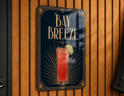 A sign for "Bay Breeze" cocktail, featuring a stylized illustration of a red drink with a lime garnish, mounted on a wooden wall.