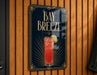 A sign for "Bay Breeze" cocktail, featuring a stylized illustration of a red drink with a lime garnish, mounted on a wooden wall.