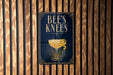 A sign that reads "BEES KNEEES" is displayed on a wooden wall.