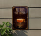 A sign with the text "BETWEEN THE SHEETS" and an illustration of a cocktail glass with a lemon peel on top, mounted on a wall next to a plant.