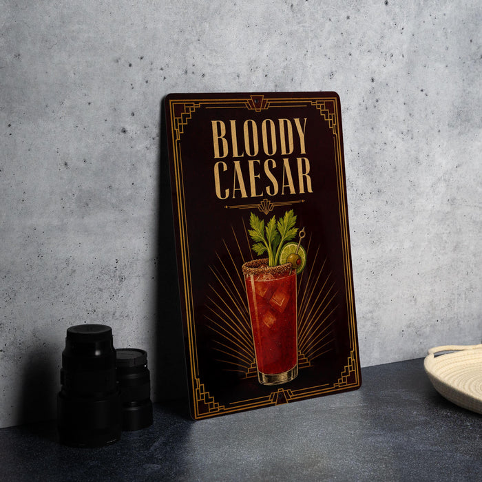 A framed poster of a Bloody Caesar cocktail is displayed on a wall, with a stack of black camera lenses and a white dish visible to the side.