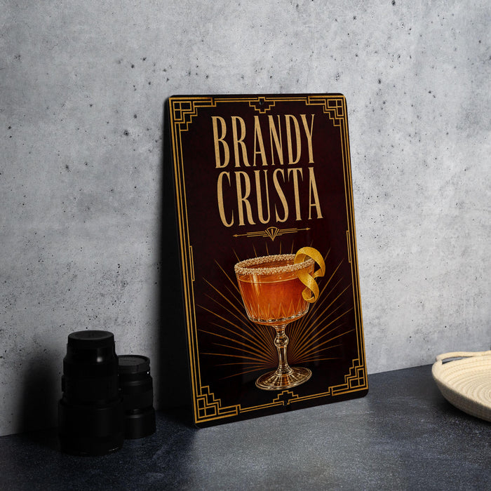 A framed advertisement for a "Brandy Crusta" cocktail, featuring an illustration of a glass filled with the drink and garnished with a lemon twist.