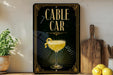a sign for a cable car, with a glass of lemonade and a lemon on the side, placed on a wooden surface next to a cutting board and some lemons.