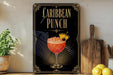 A decorative sign for a Caribbean punch cocktail, featuring a glass of the drink with a pineapple and a cherry on top, along with a wooden cutting board and a potted plant in the background.