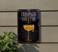 A sign advertising a champagne cocktail is displayed on a wall, featuring an illustration of a champagne glass with a lemon twist.