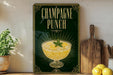 A sign for "Champagne Punch" is displayed on a shelf, accompanied by a potted plant, a cutting board, and some lemons.