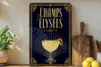 A framed poster with the text "CHAMPS ELYSEES" and an illustration of a cocktail glass with a lemon twist.