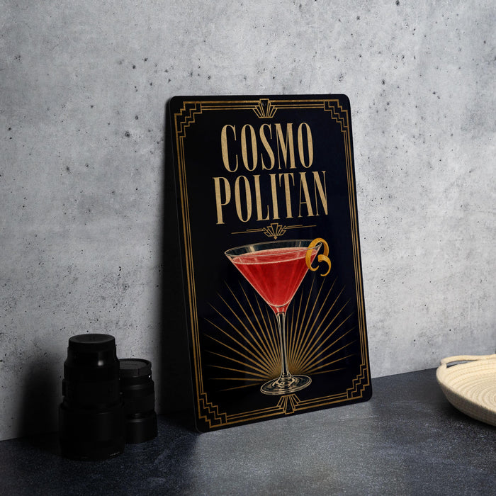 A decorative sign for a cocktail called "Cosmo Politan" is displayed on a table, featuring an illustration of a martini glass with a red drink and a lemon twist.