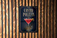 A sign for a cocktail called "Cosmo Politan" is displayed on a wooden wall.