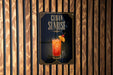 A sign for "Cuba Sunrise" cocktail, featuring an illustration of a colorful drink with a garnish and a straw.