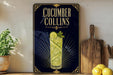 a decorative sign for a cucumber Collins cocktail, with a glass of the drink and garnish visible.