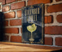 A sign for a cucumber gin cocktail is displayed on a brick wall.