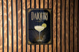 A sign for "Daiquila" is displayed on a wooden wall, featuring an illustration of a cocktail glass with a lime slice.
