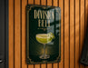 A sign for "Division Bell" cocktail, featuring a stylized illustration of a cocktail glass with a lemon twist on a green background.