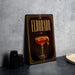 A framed poster of a cocktail called "Eldorado" is displayed on a wall, featuring an illustration of a glass filled with a red drink and a lemon twist.