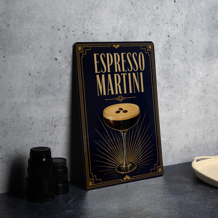 A framed poster of an espresso martini is displayed on a gray countertop, with a stack of black cups and a white dish visible to the side.