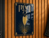 A sign with the text "FRENCH 75" and an illustration of a champagne glass is displayed on a wooden wall.