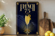 A framed poster with a champagne glass and a lemon on a wooden shelf, surrounded by kitchen utensils and a potted plant.