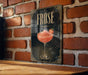 a framed poster of a pink cocktail glass with a strawberry garnish, mounted on a brick wall.