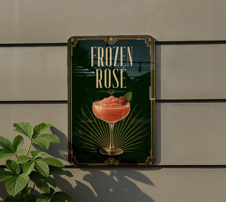 A sign for a frozen rose cocktail is displayed on a wall, with a plant visible to the left.