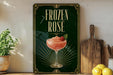 A framed poster advertising a "FROZEN ROSE" cocktail, featuring a glass of pink drink with a strawberry garnish.