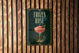 A sign for a frozen rose cocktail is displayed on a wooden wall.