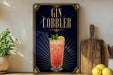 A framed poster advertising a Gin Cobbler cocktail, featuring a glass of the cocktail with a lemon slice and mint leaves.