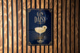 A decorative sign with the text "GIN DAISY" and an illustration of a cocktail glass with a flower on it, mounted on a wooden wall.