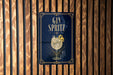 A sign for a gin cocktail called "Spritz" is displayed on a wooden wall.
