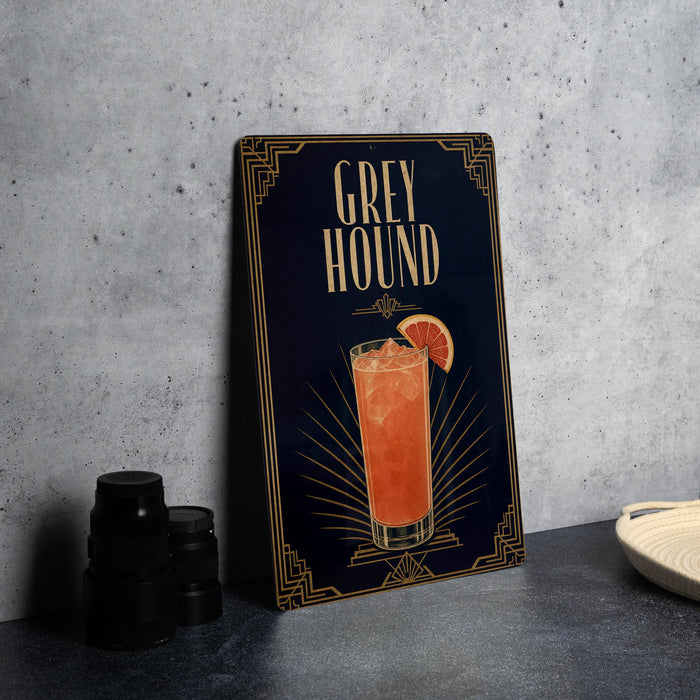 A decorative sign for a cocktail called "Greyhound" is displayed on a table, featuring an illustration of a cocktail glass with a slice of orange.
