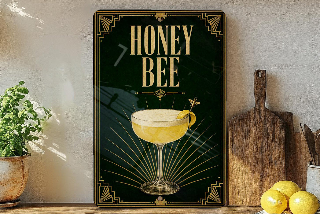 A framed poster with the text "HONEY BEE" and an illustration of a cocktail glass with a lemon twist, placed on a wooden shelf next to a wooden cutting board and a potted plant.