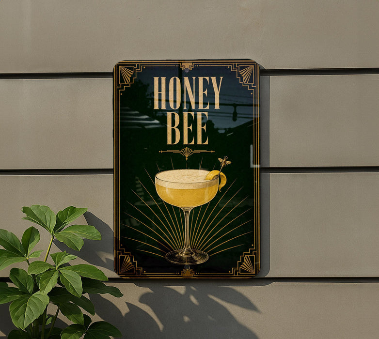A sign for a honey bee cocktail is displayed on a wall, with a plant visible to the left.
