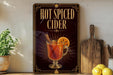 A framed advertisement for hot spiced cider is displayed on a wall, featuring an illustration of a glass of hot spiced cider with a slice of orange.