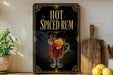 A framed advertisement for "Hot Spiced Rum" featuring an illustration of a glass of hot rum with a slice of lemon and a cinnamon stick.