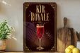 a decorative sign for a beverage called "Kir Royale", with a glass of red liquid and a garnish on the sign.