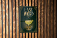 A sign with the text "LAST WORD" and an illustration of a cocktail glass is displayed on a wooden wall.