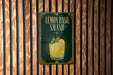A sign for a lemon basil smash cocktail is displayed on a wooden wall.