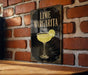 A framed poster of a lime margarita on a brick wall, featuring a stylized illustration of a margarita glass with a lime slice.