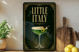 a framed poster with a green cocktail glass and a lemon twist, placed on a shelf next to a wooden cutting board and a potted plant.