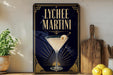 A framed advertisement for Lychee Martini, featuring a martini glass with a lemon twist on a dark background with a sunburst design.