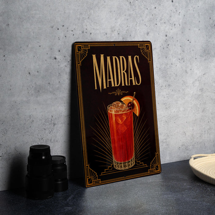 A framed poster of a Madras cocktail is displayed on a wall, with a stack of black camera lenses and a white dish visible to the side.