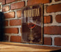 A framed poster of a Manhattan cocktail is displayed on a brick wall.